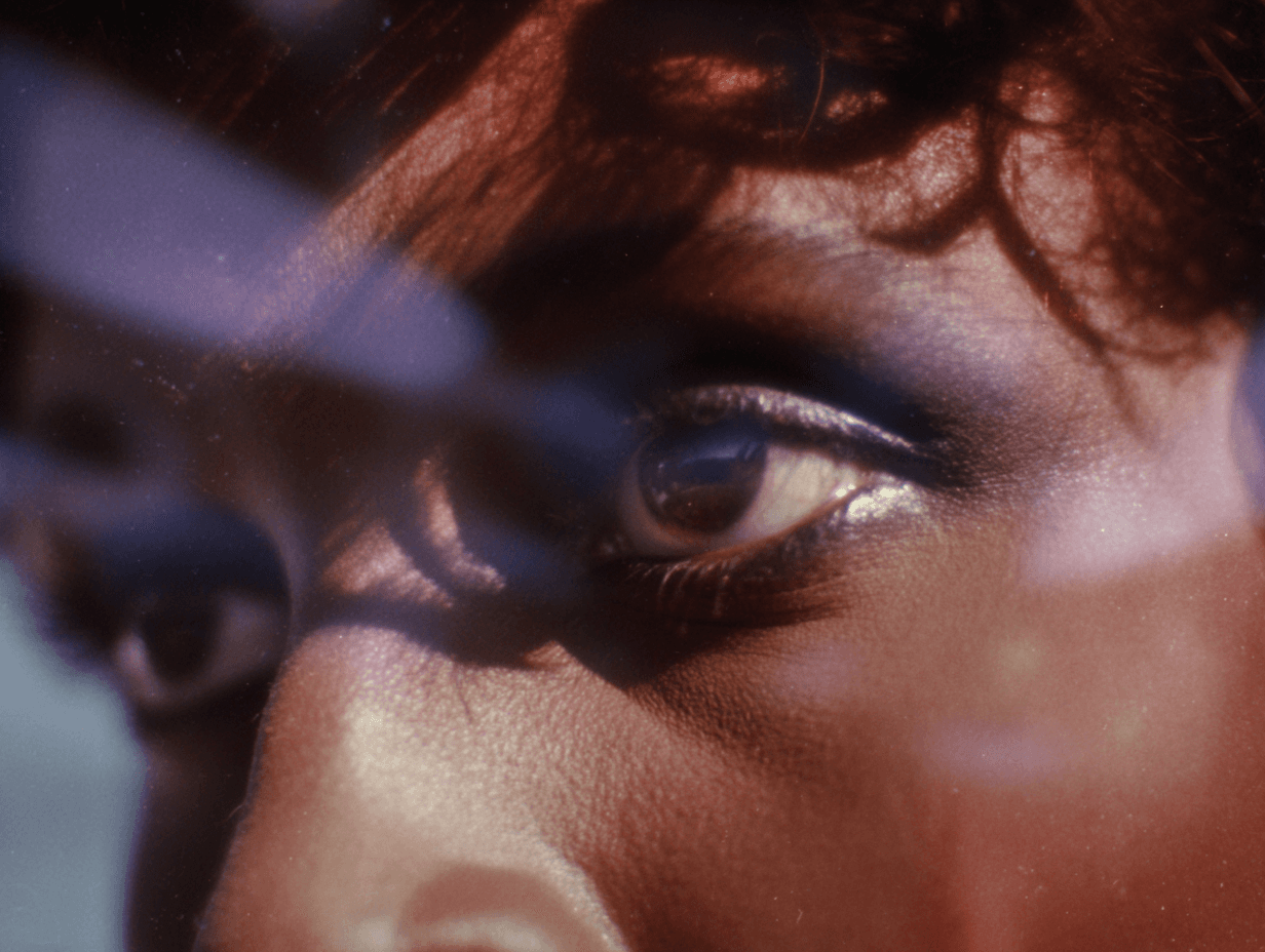 Macro of a heavily made-up eye through a gauze of red sequin glitter, blue eye iris, painterly bokeh